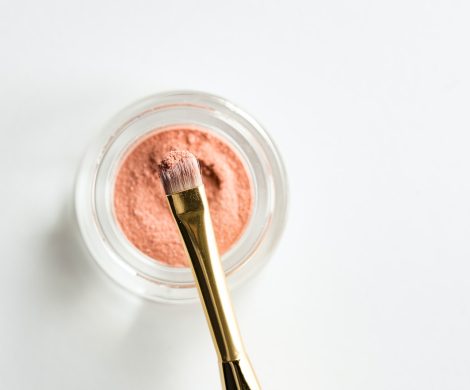 brown makeup brush in front pink powder on glass case